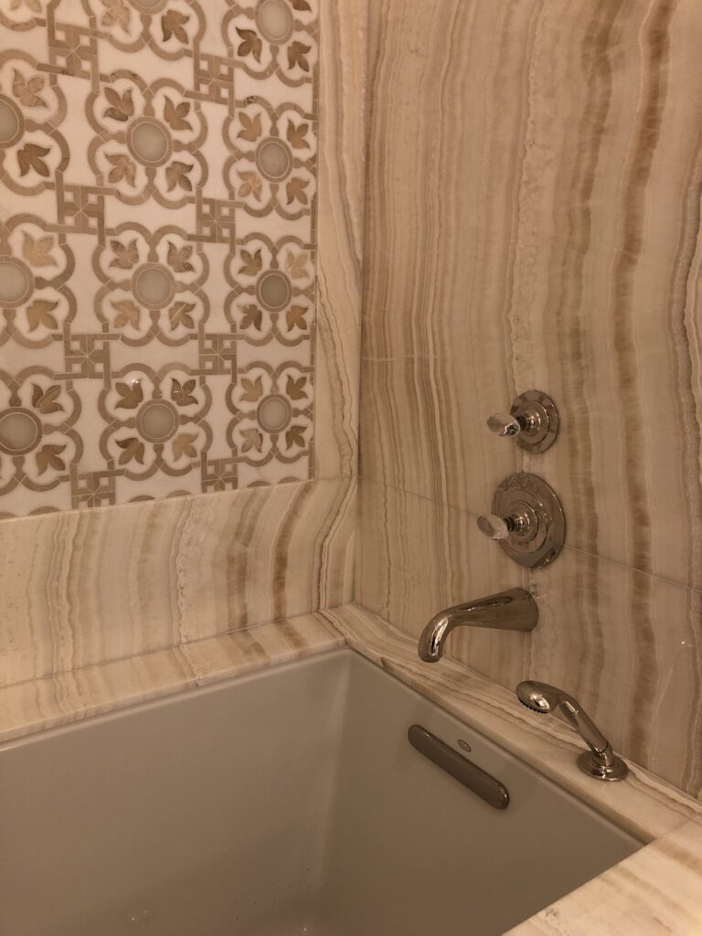 Her Bathroom bathtub top and walls in Ivory onyx slab and custom mosaic